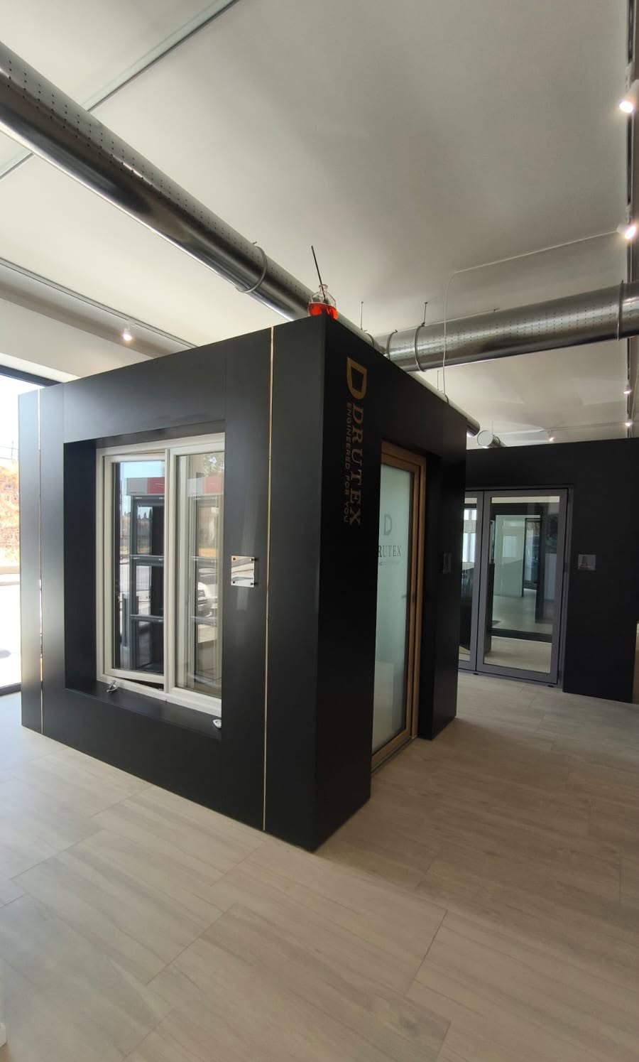 Cubo espositivo nero con scritta Drutex, finestra bianca e porta vetrata in legno nello showroom VG Infissi