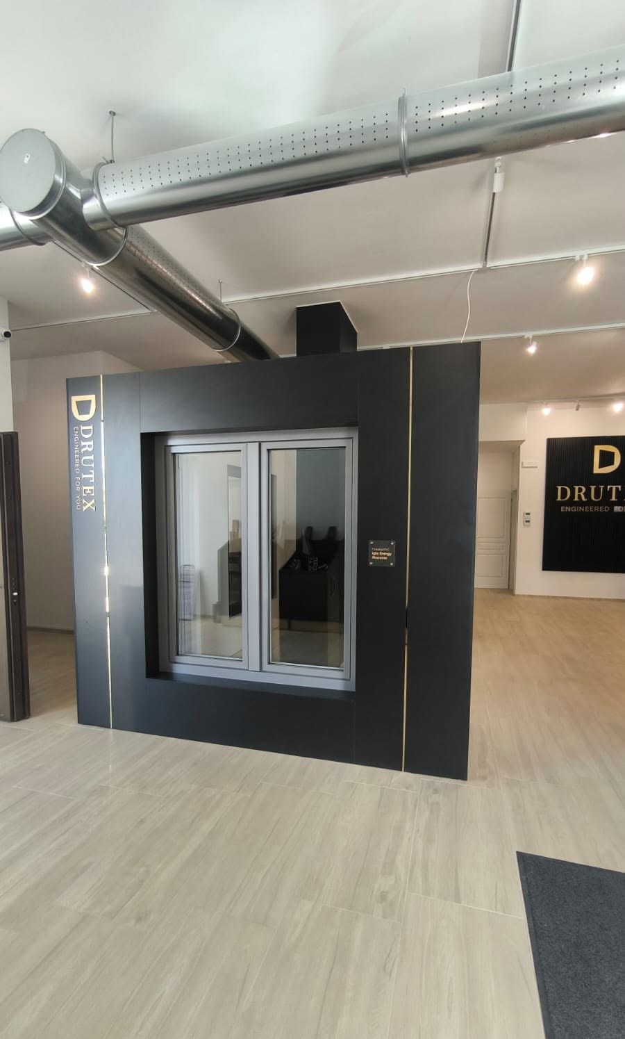 Finestra a due ante con telaio grigio su espositore nero Drutex con filetti dorati nello showroom VG Infissi