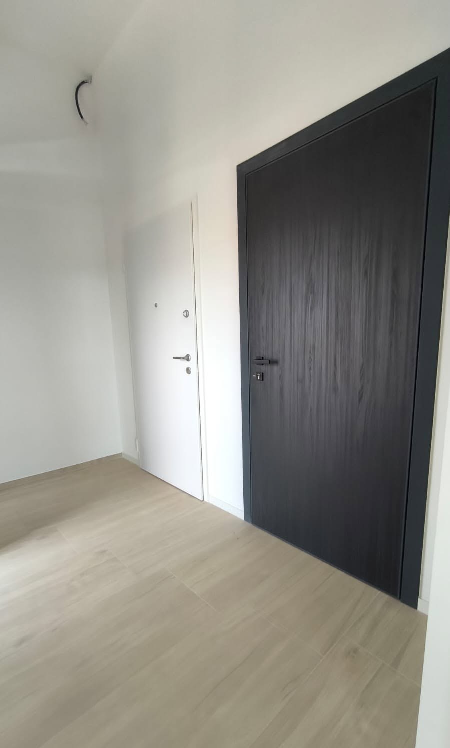 Portoncino bianco con spioncino accanto a porta interna effetto legno scuro, su pavimento chiaro in un ingresso vuoto